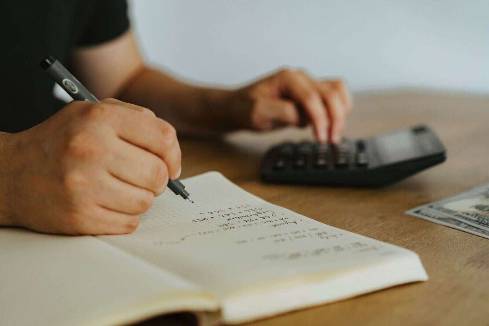 Manos anotando cálculos en un cuaderno junto a una calculadora