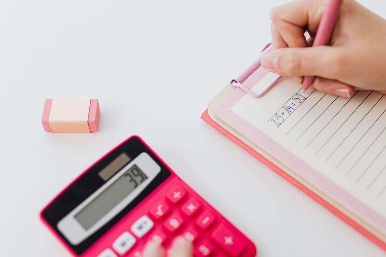 Manos escribiendo números en un cuaderno junto a una calculadora