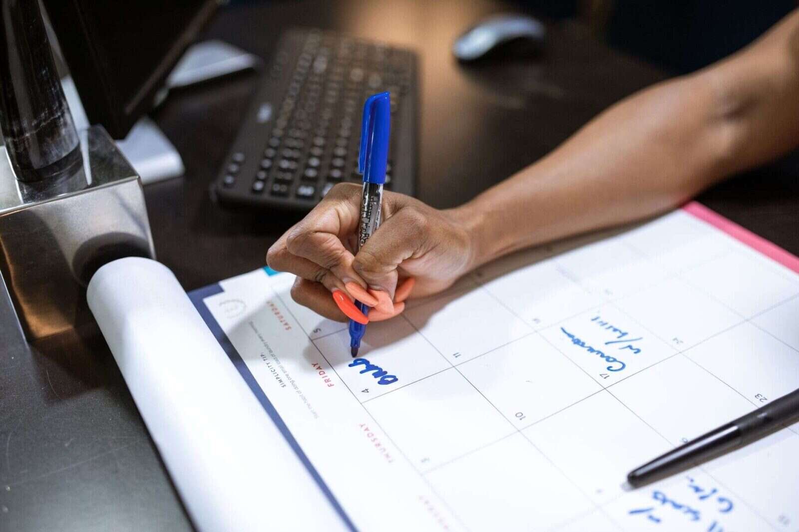 Mano anotando fechas con un rotulador azul en un calendario