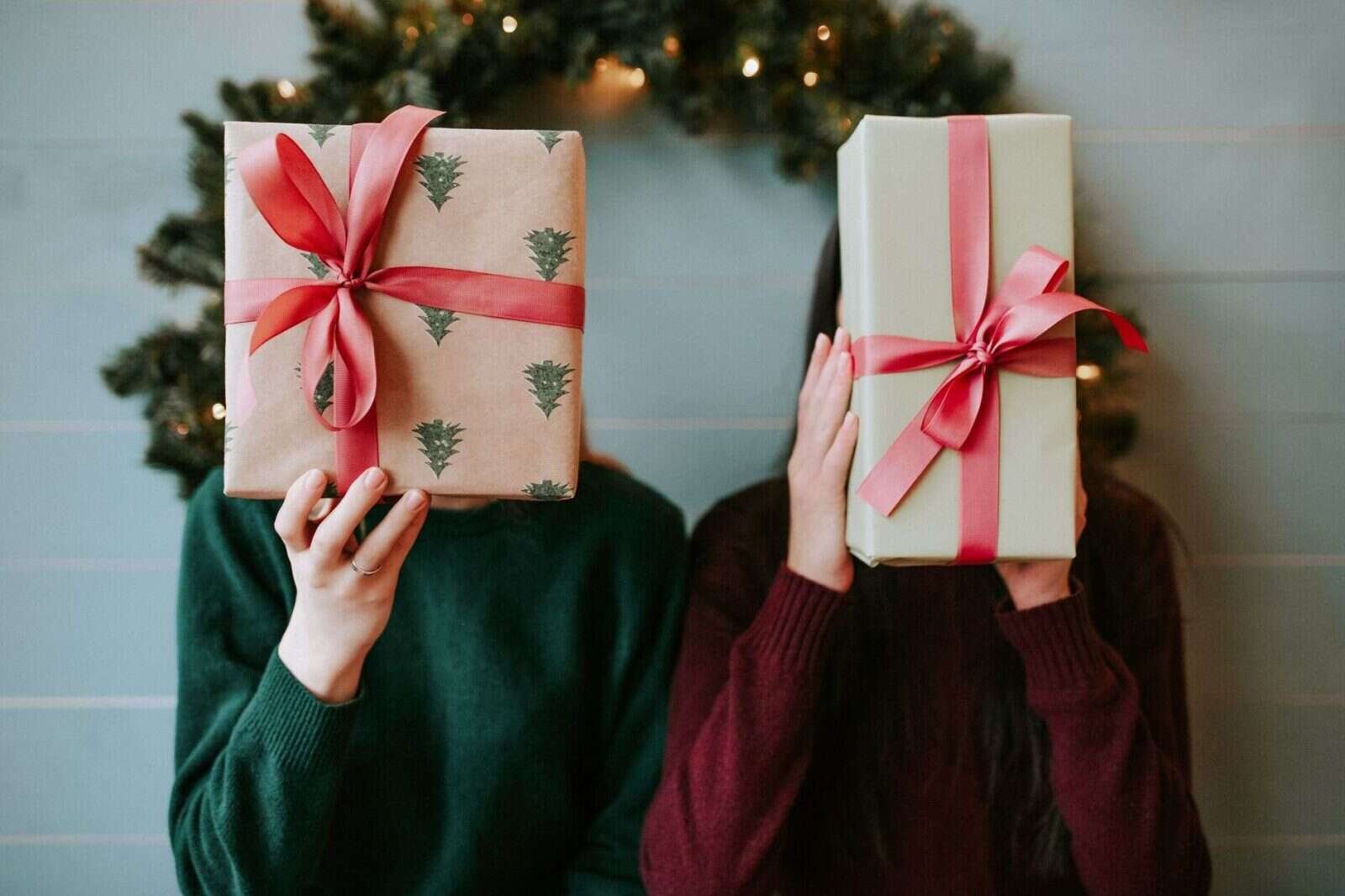 Dos personas sosteniendo regalos junto a una corona navideña