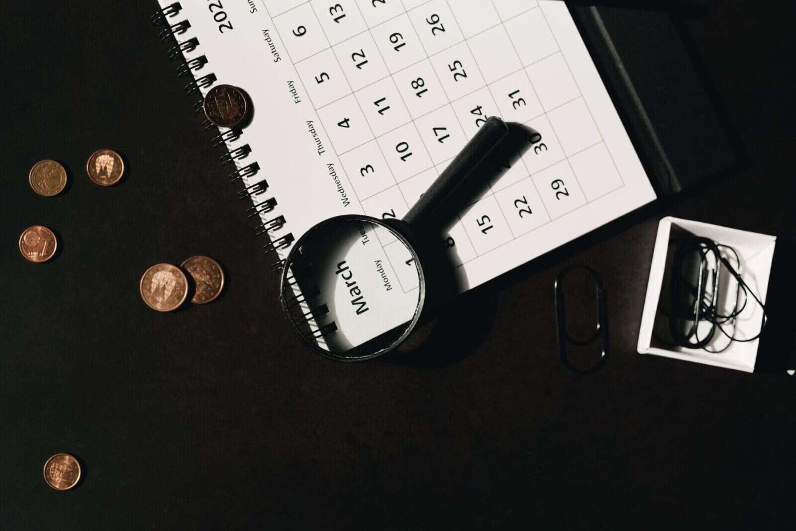 Calendario con una lupa y monedas sobre la mesa