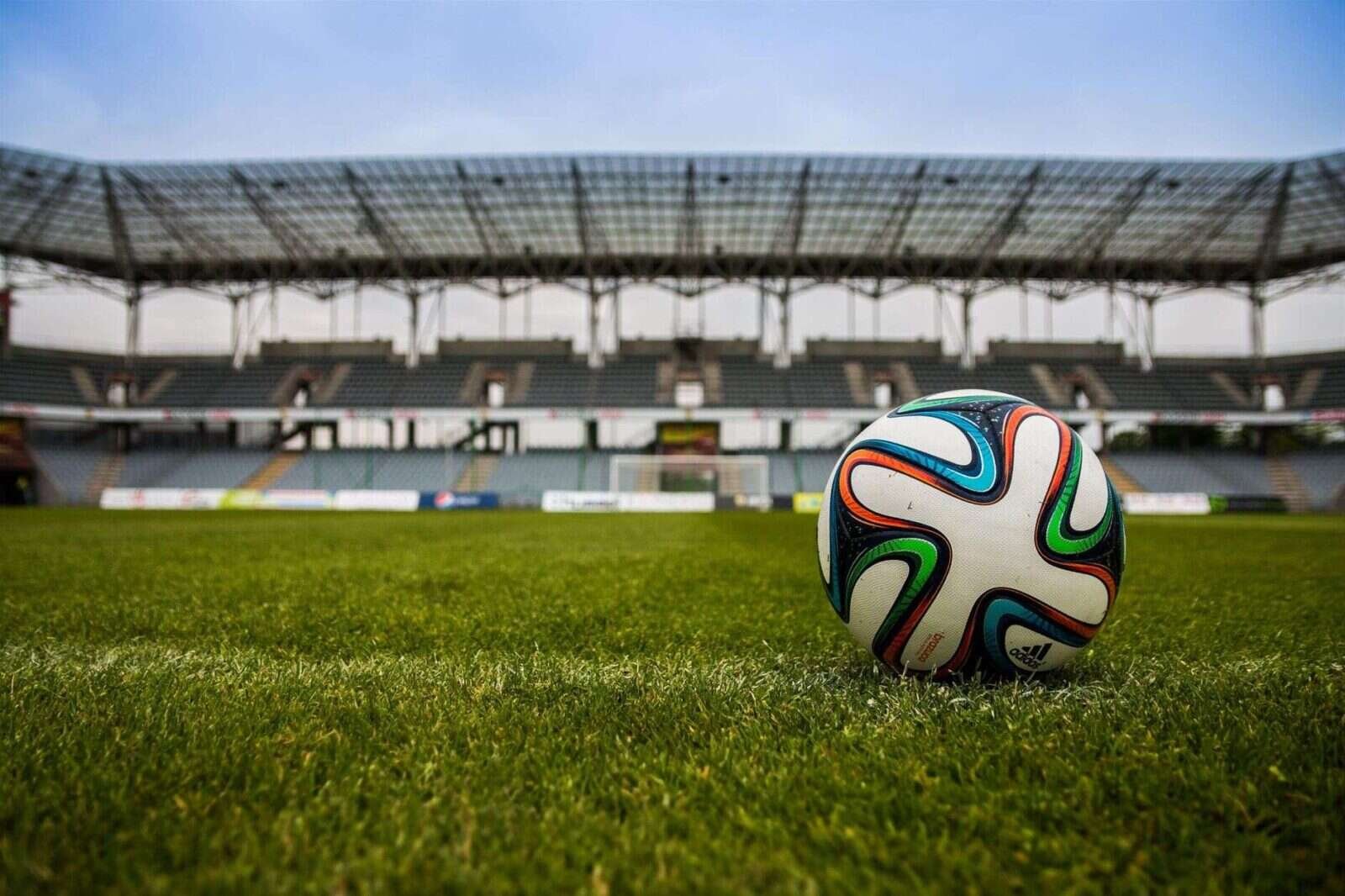 Balón de fútbol sobre el césped con un estadio vacío al fondo